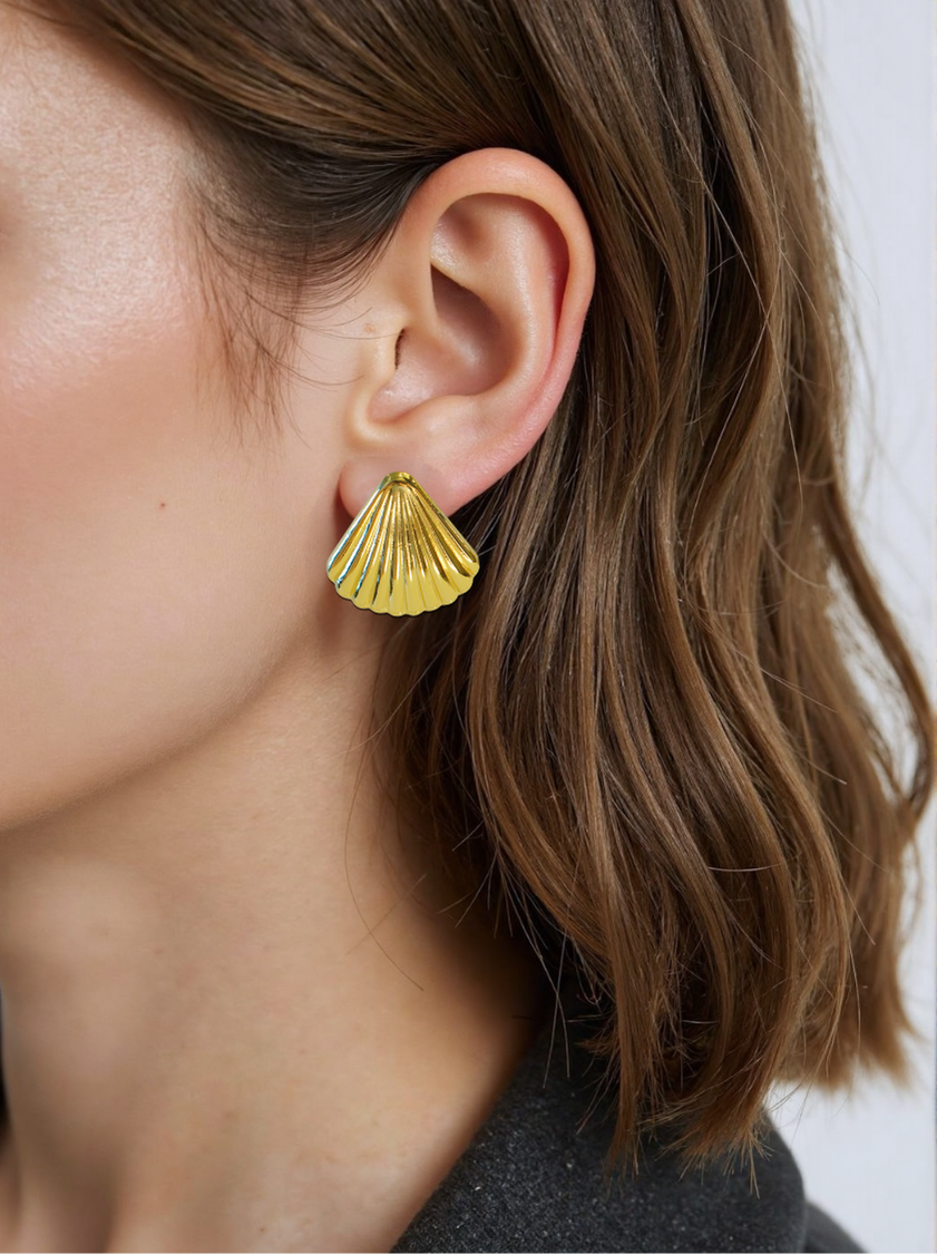 A close-up of a woman wearing gold shell stud earrings, featuring a vintage-inspired seashell design with a polished finish. The earrings add an elegant coastal charm to her outfit.