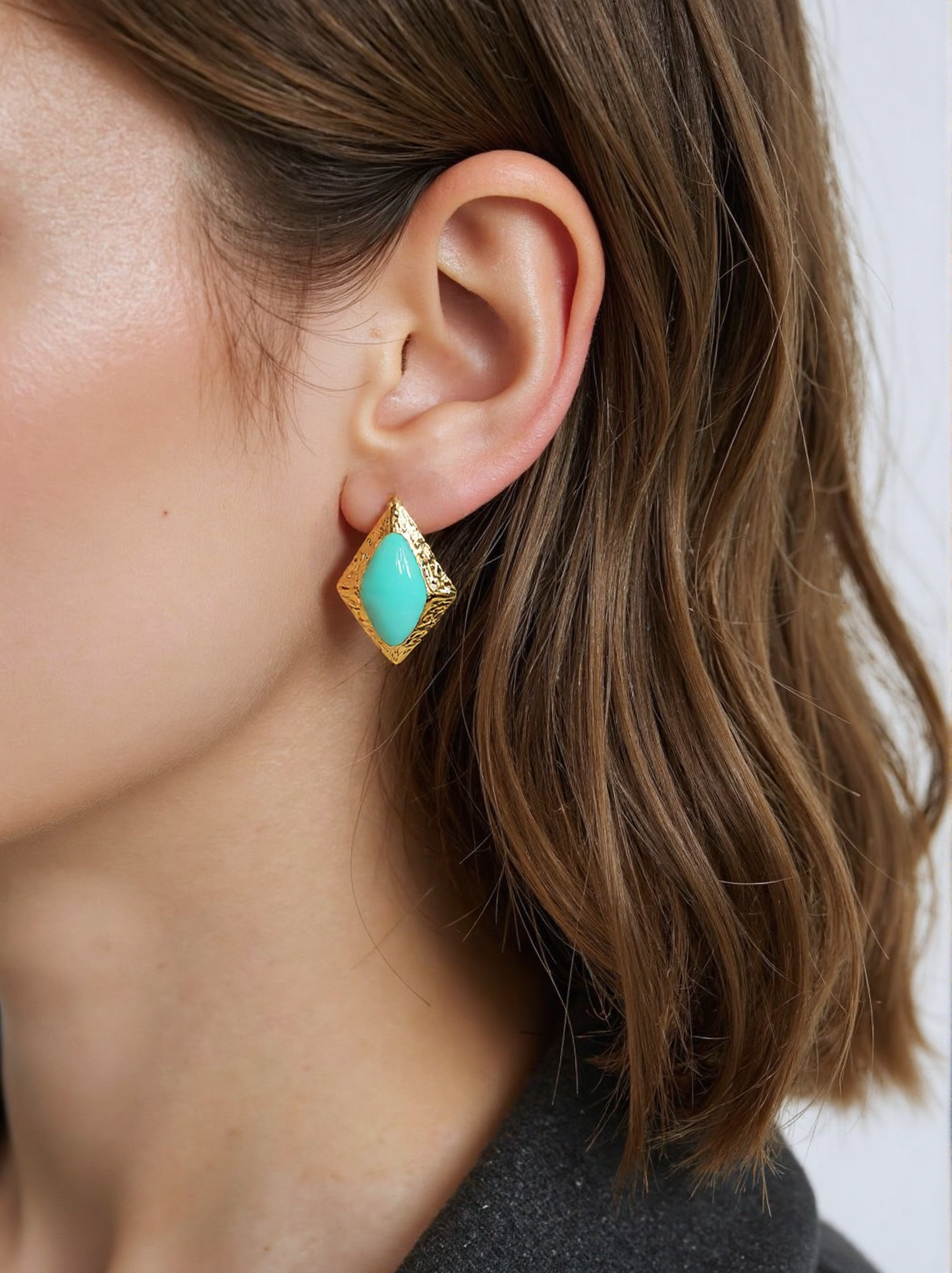 A woman wearing gold and turquoise geometric stud earrings, featuring a textured gold frame and vibrant turquoise stone. These vintage-inspired statement earrings add a bold and elegant touch to her outfit.