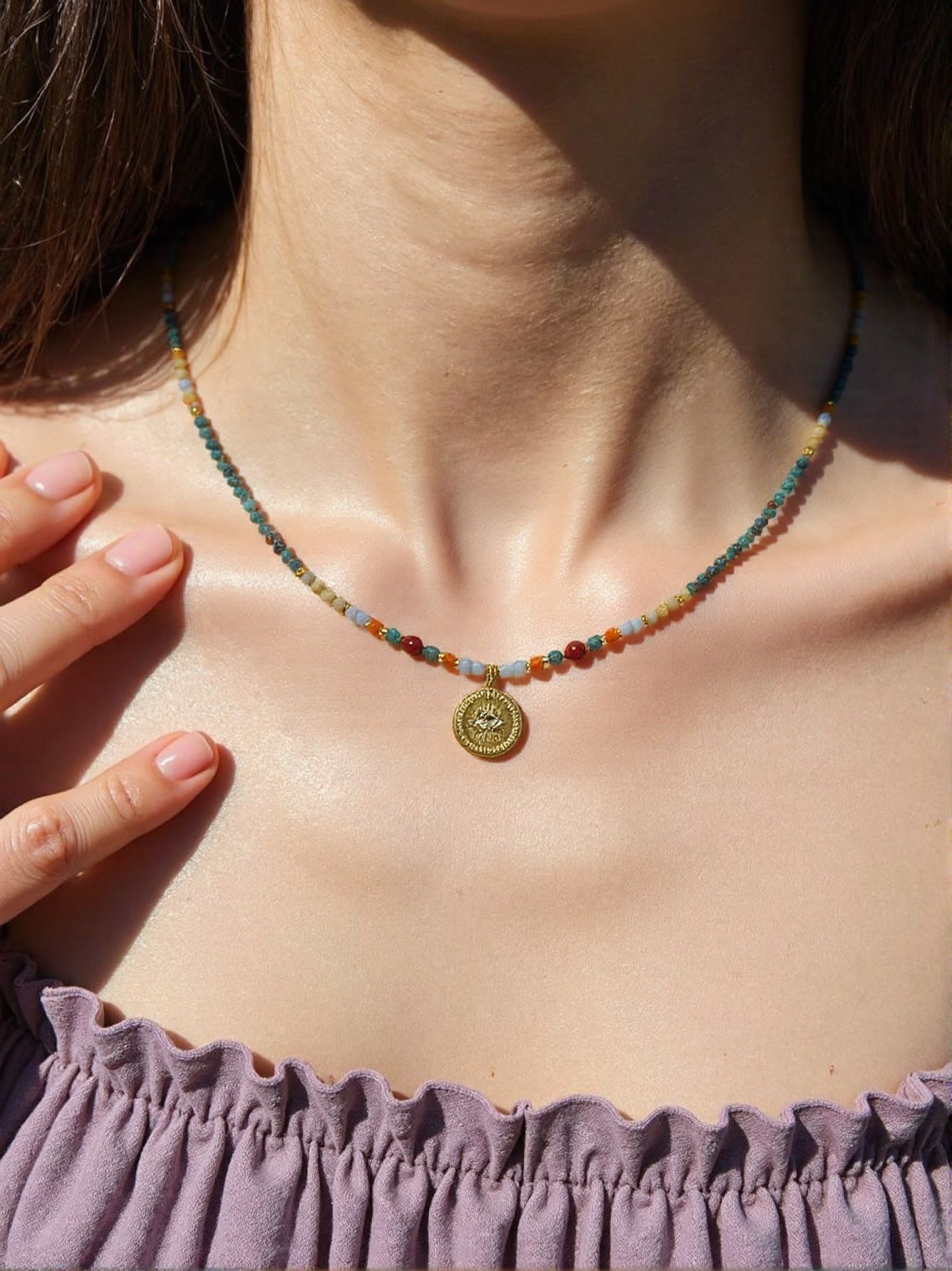 Colorful gemstone beaded necklace with gold medallion pendant on woman’s neck