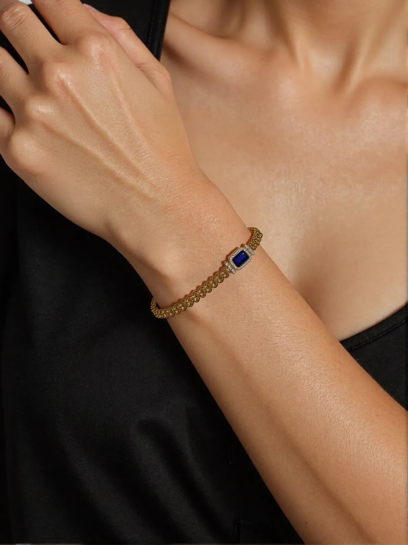 Gold bracelet with emerald-cut blue gemstone on woman’s wrist