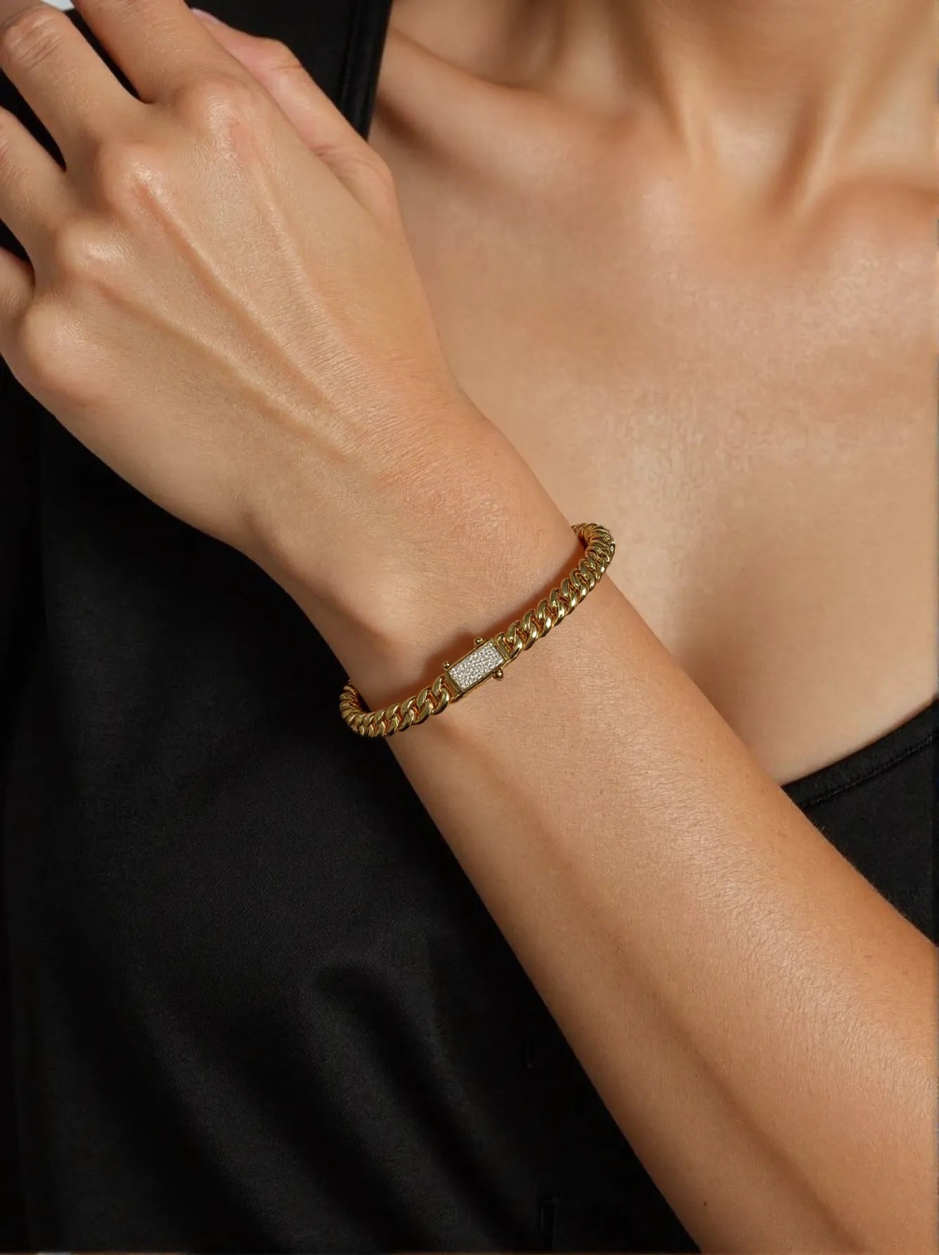 Chunky gold chain bracelet with diamond-studded clasp on woman’s wrist