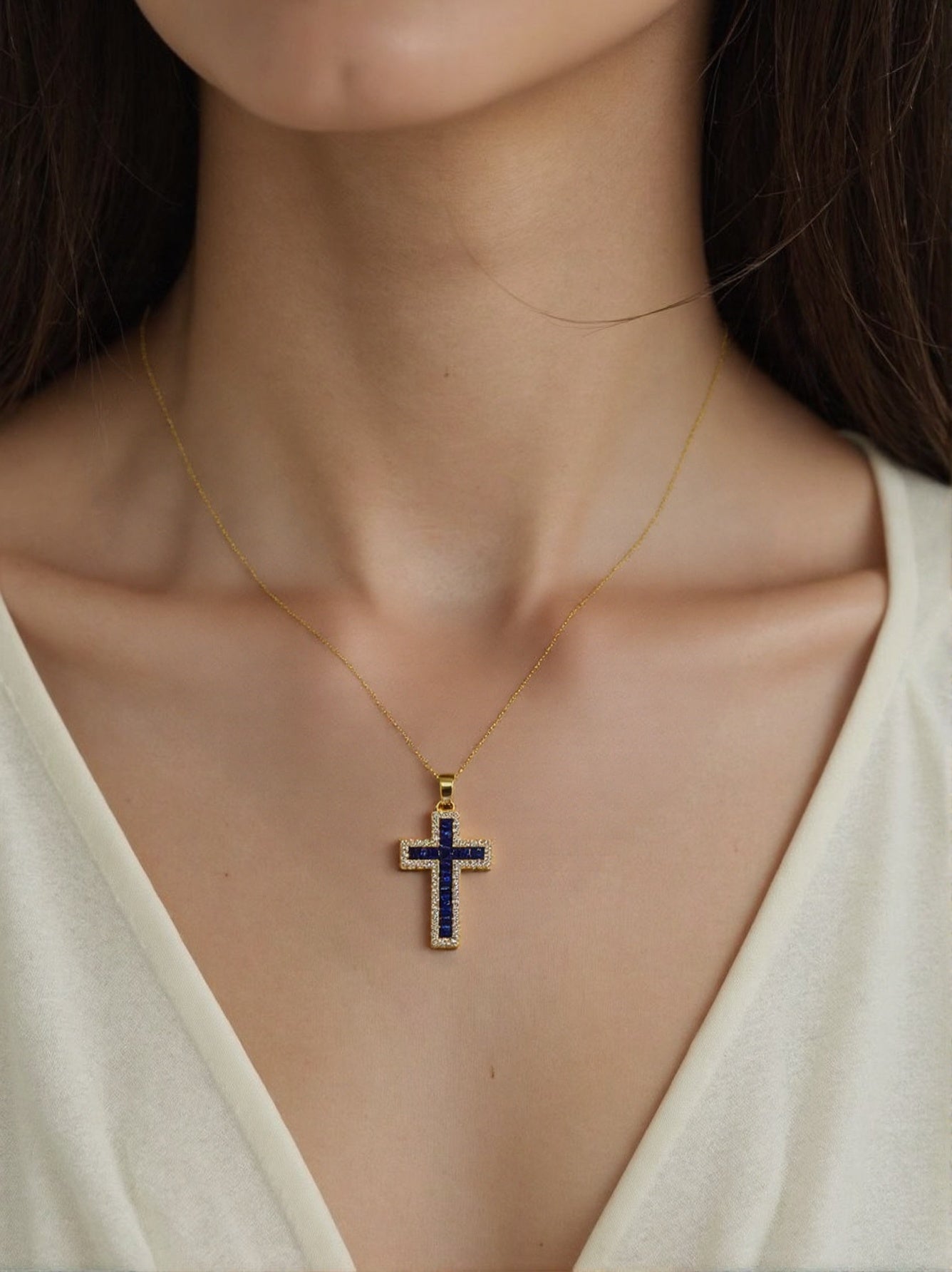 Gold necklace with deep blue diamond cross pendant on woman’s neck