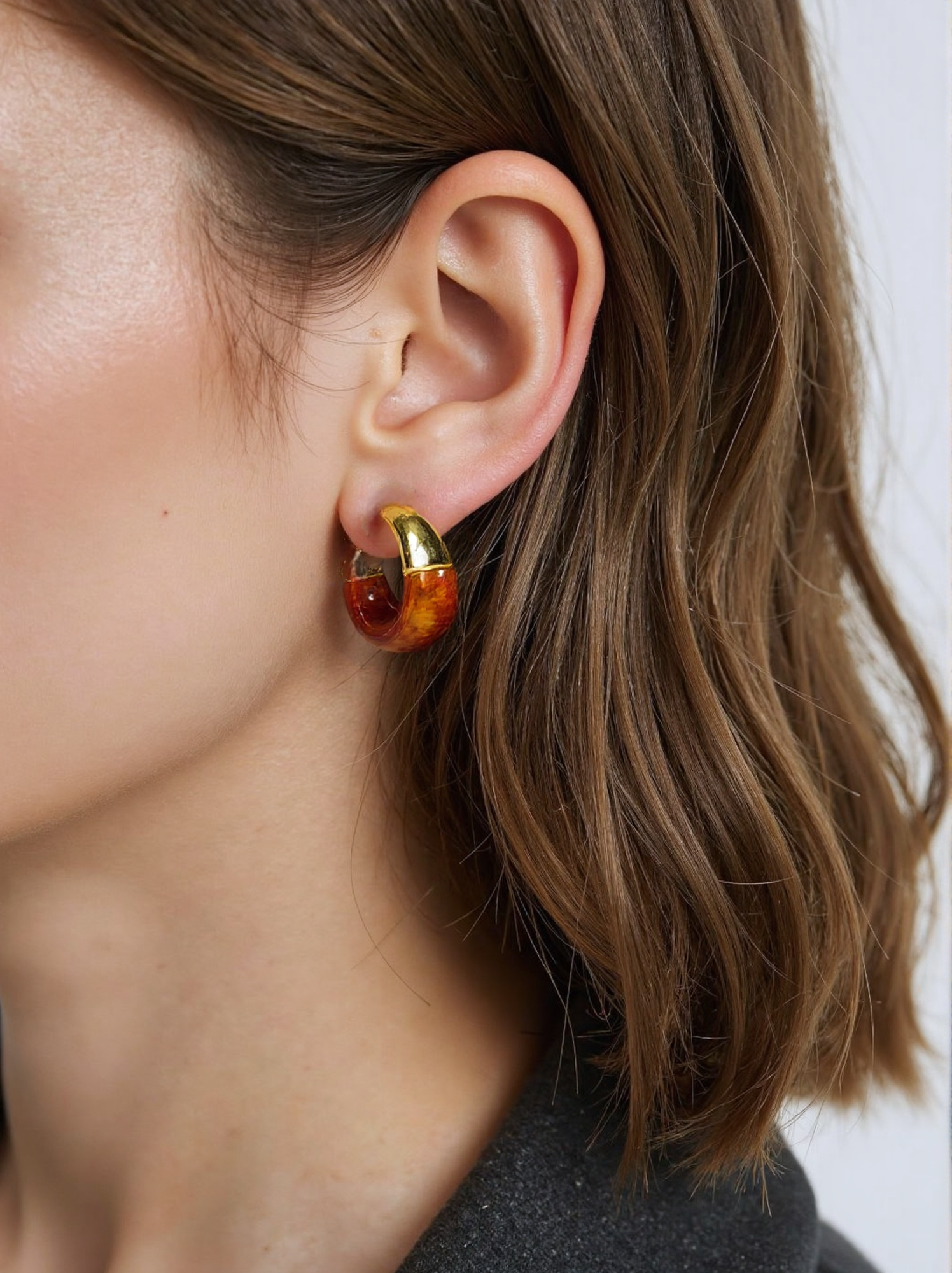 A woman wearing amber resin and gold hoop earrings, featuring a chunky vintage-inspired design with a glossy finish. These statement earrings add a bold yet sophisticated touch to her outfit.