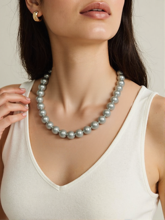 A woman wearing a classic gray pearl necklace featuring round simulated pearls, styled elegantly with a white sleeveless top and gold earrings.