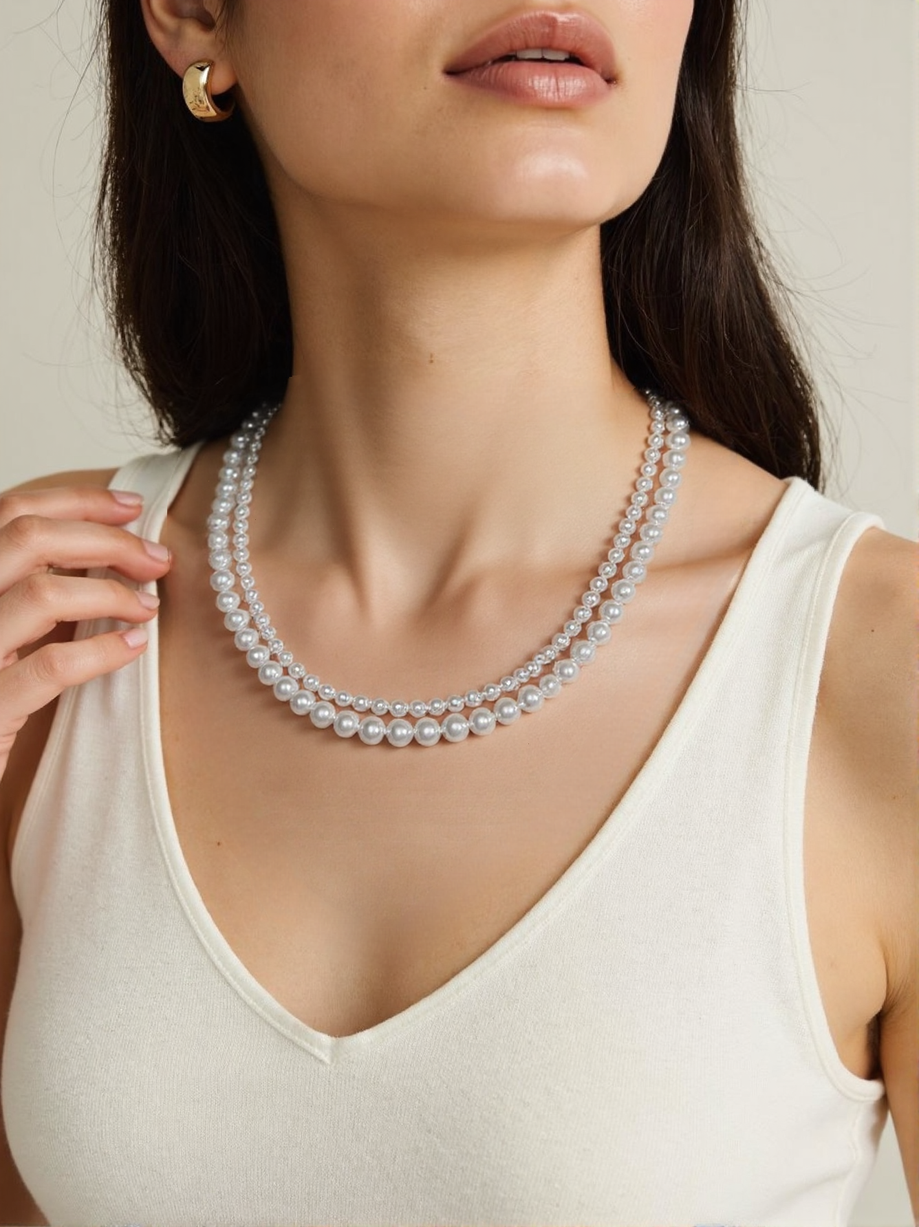 A woman wearing a double-layer white pearl necklace with high-quality simulated pearls, styled elegantly with a white sleeveless top and gold earrings.