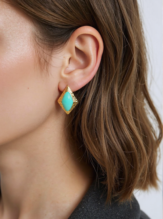 A woman wearing gold and turquoise geometric stud earrings, featuring a textured gold frame and vibrant turquoise stone. These vintage-inspired statement earrings add a bold and elegant touch to her outfit.