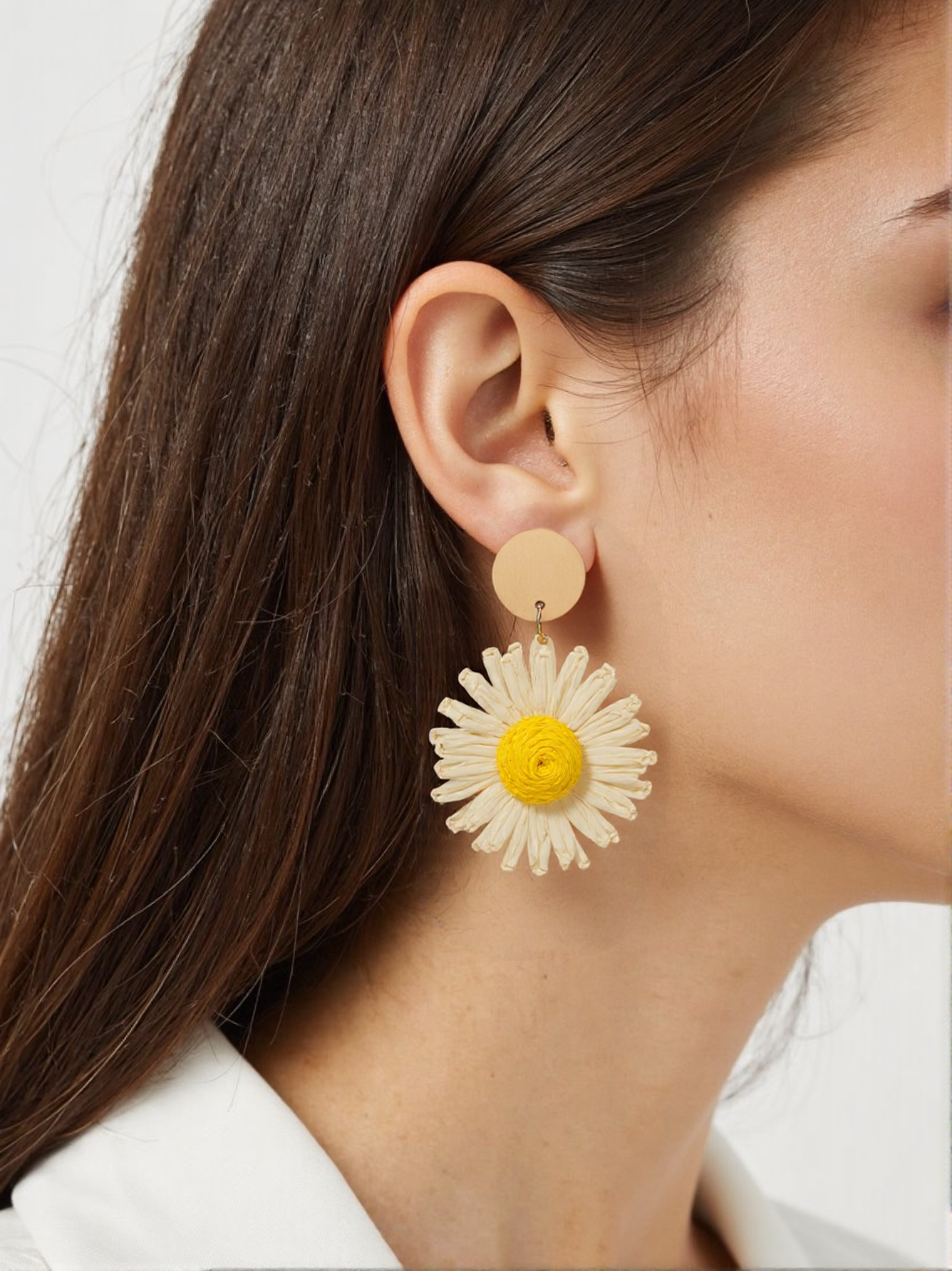A woman wearing handmade woven daisy earrings, featuring a raffia flower design with a bold yellow center. These lightweight boho floral earrings add a playful and nature-inspired touch to her outfit.