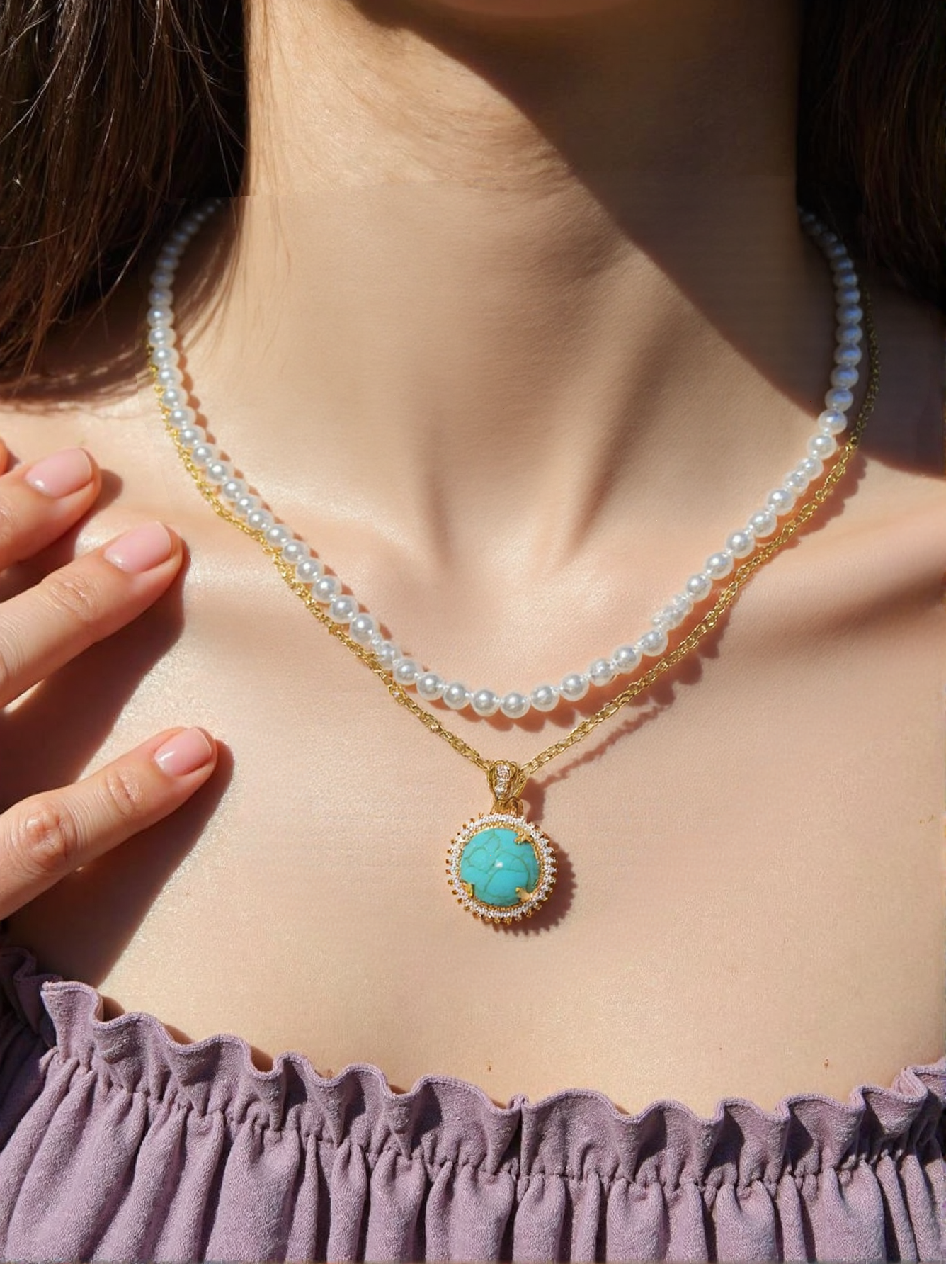 A woman wearing a layered pearl and gold chain necklace with a round turquoise pendant, styled elegantly with a purple off-shoulder top in natural sunlight.