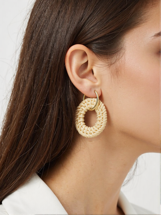 A woman wearing woven rattan hoop earrings, featuring a handwoven circular design with gold accents. These lightweight bohemian earrings add an effortless, nature-inspired touch to her outfit.