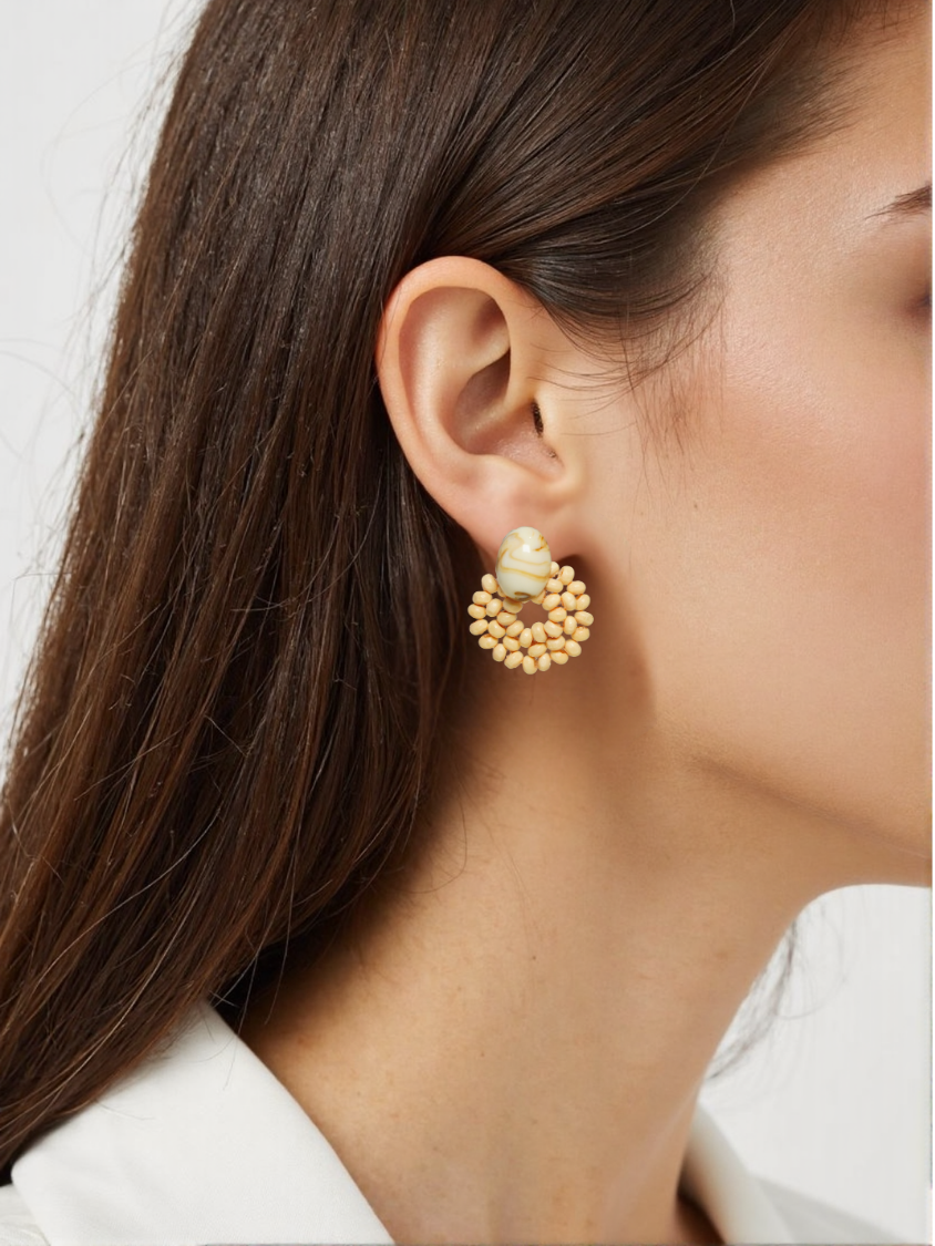 A woman wearing woven rattan and resin statement earrings, featuring a marbled resin stud and handwoven rattan beads in a circular shape. These bohemian-inspired earrings add a natural and earthy touch to her outfit.