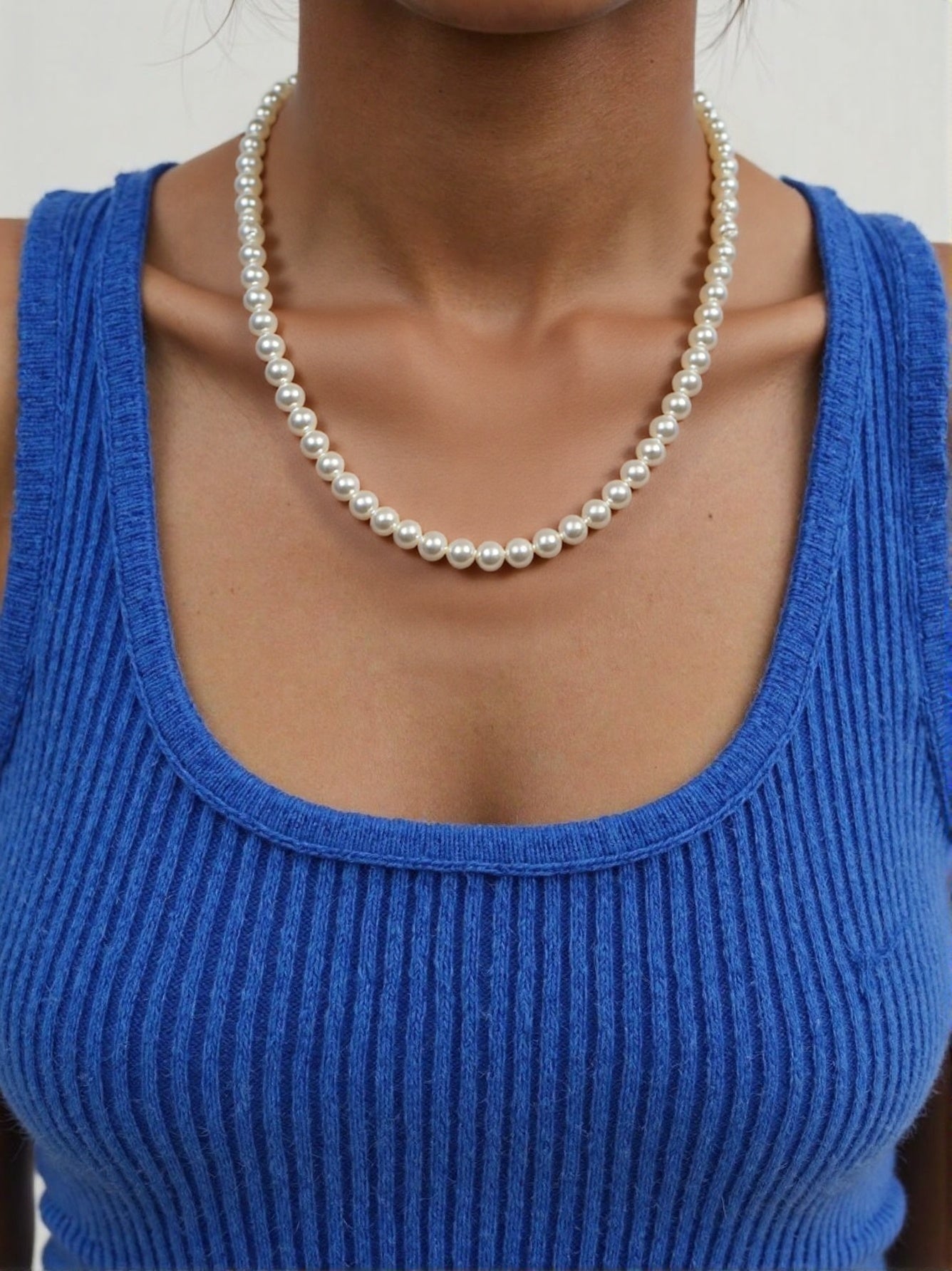 Classic single-strand pearl necklace on woman wearing blue top 