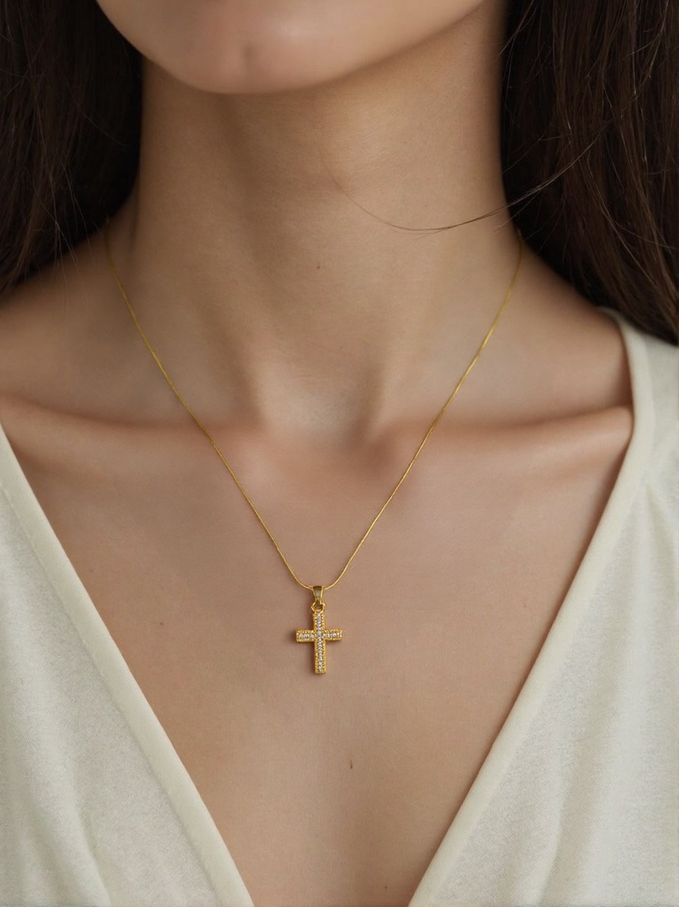 Minimalist gold necklace with small diamond cross pendant on woman’s neck