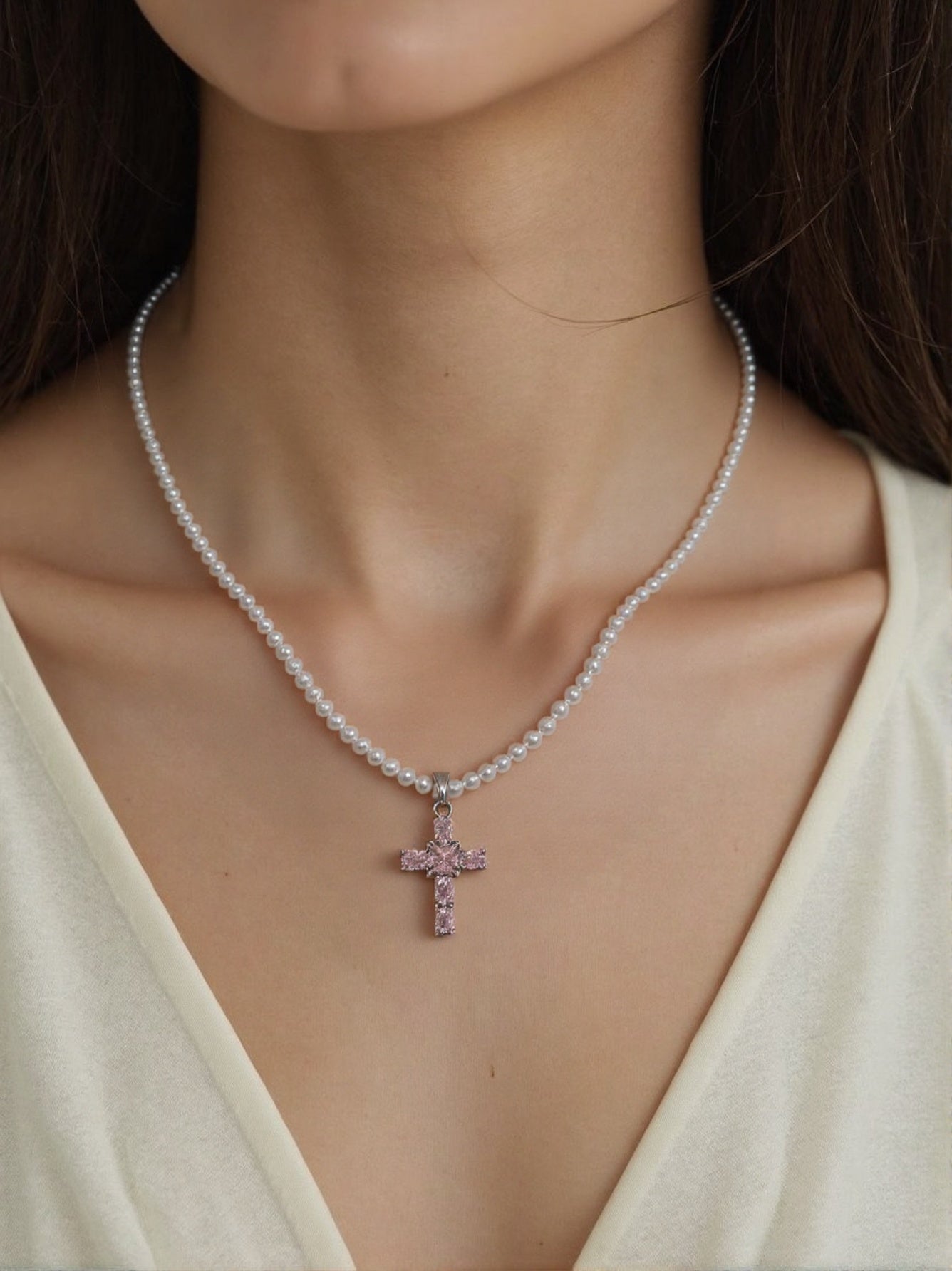 Pearl necklace with pink diamond cross pendant on woman’s neck
